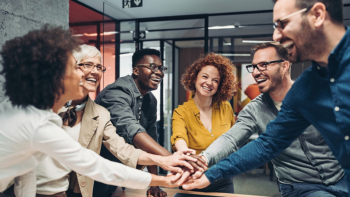 Group of coworkers huddling while stacking their hands to prepare to celebrate.