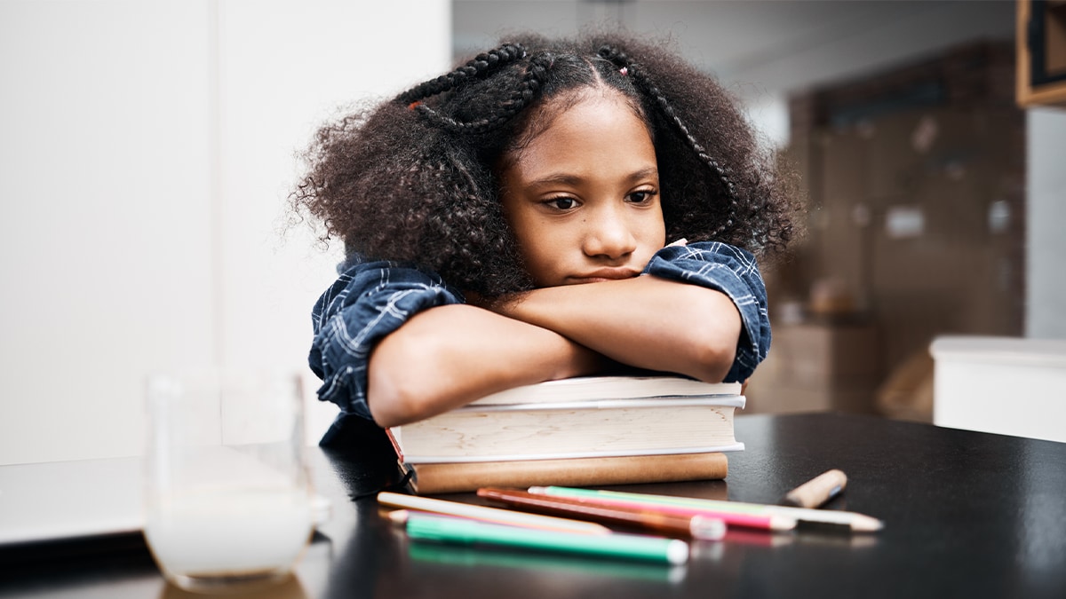 The child is putting her arms on top of her books, frustrated