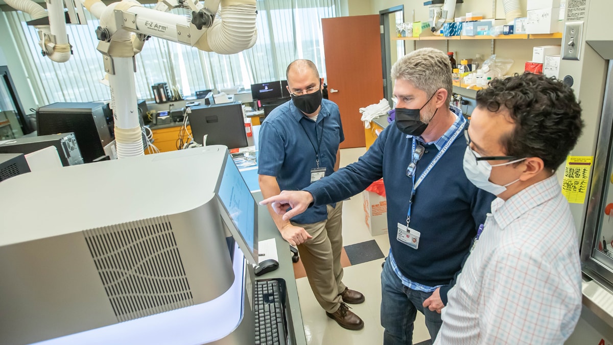 3 men in talking in a lab