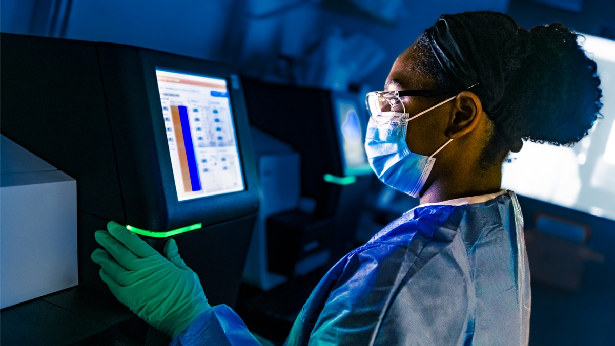 CDC scientist in protective gear views information on a sequencer. The glow from the screen illuminates her face.