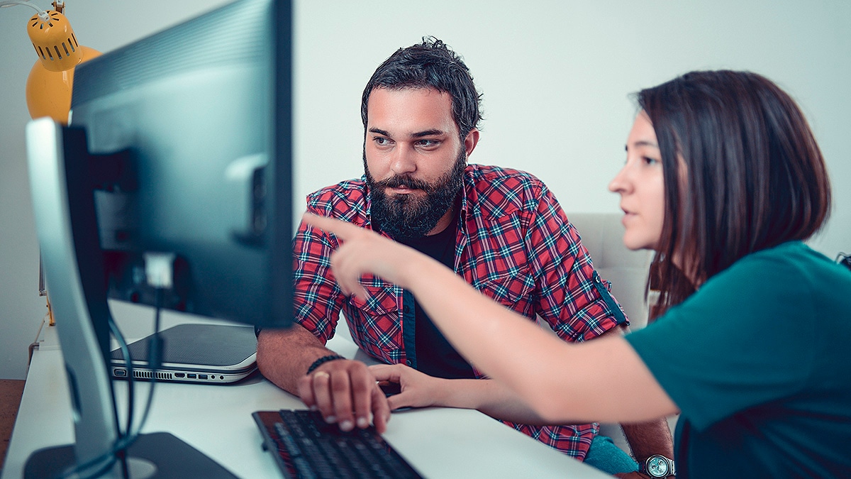 Two people working together on a project. One person pointing at computer monitor.