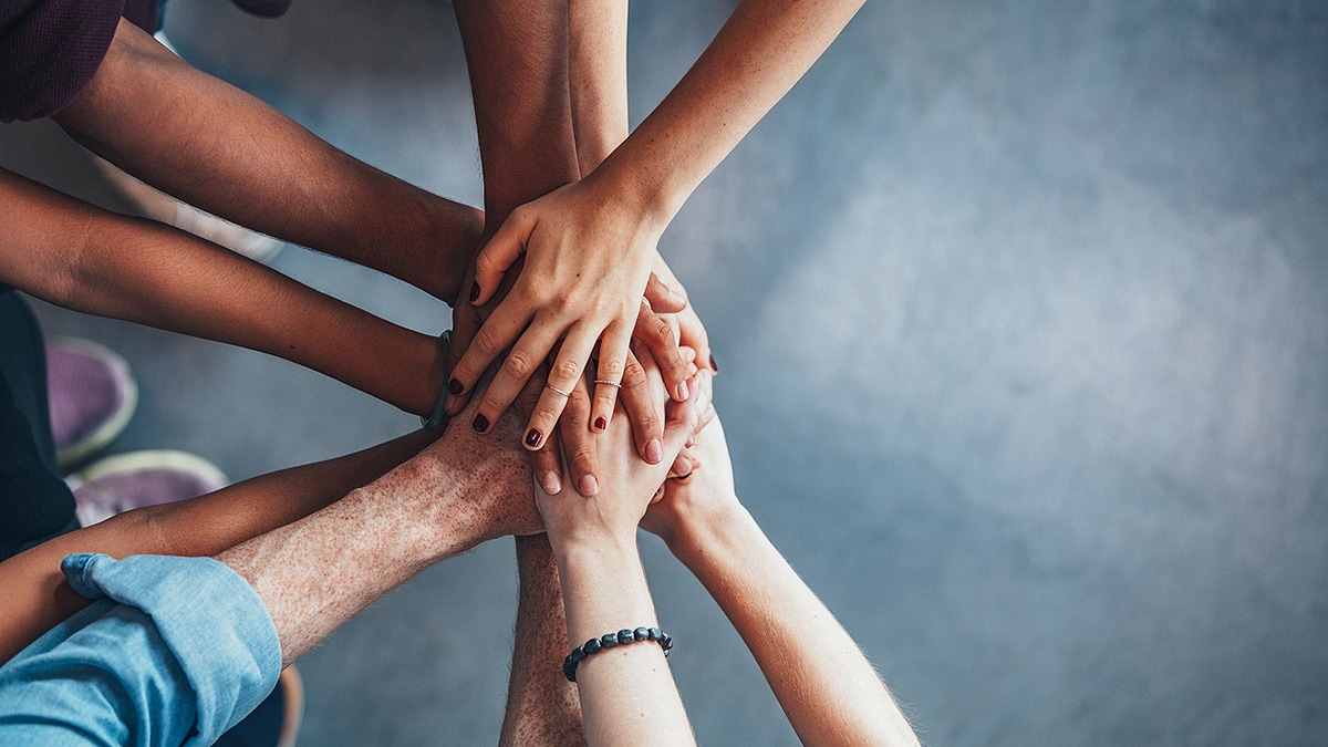 Many hands join together in the center of a circle to demonstrate teamwork and collaboration.