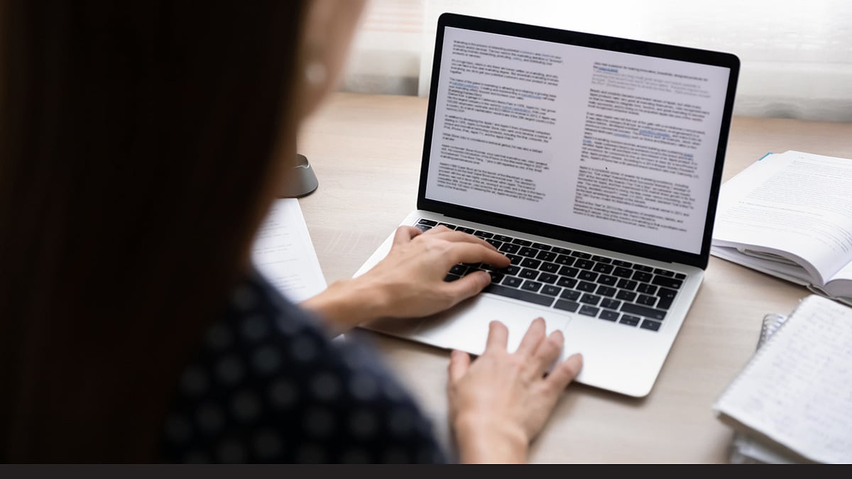 Over-the-shoulder photo of young business woman concentrating on electronic documents via laptop.