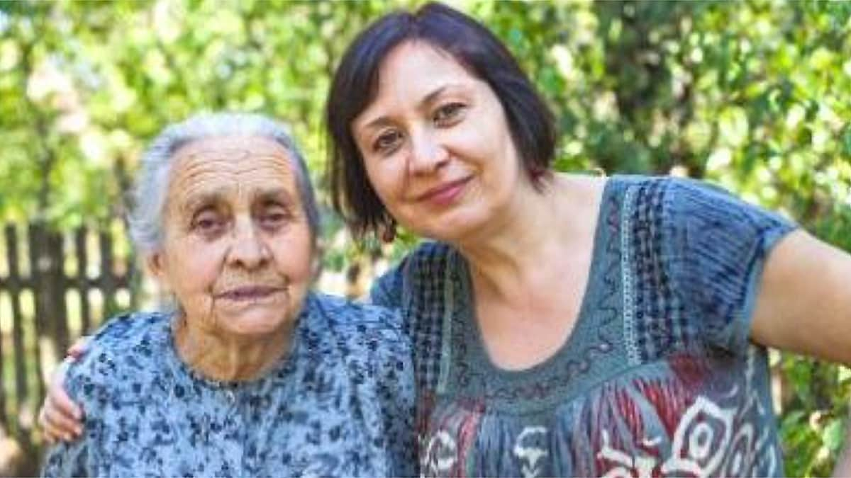 An older Hispanic woman with gray hair (on left), arm in arm with and a middle-aged Hispanic woman with short, black hair (on right).