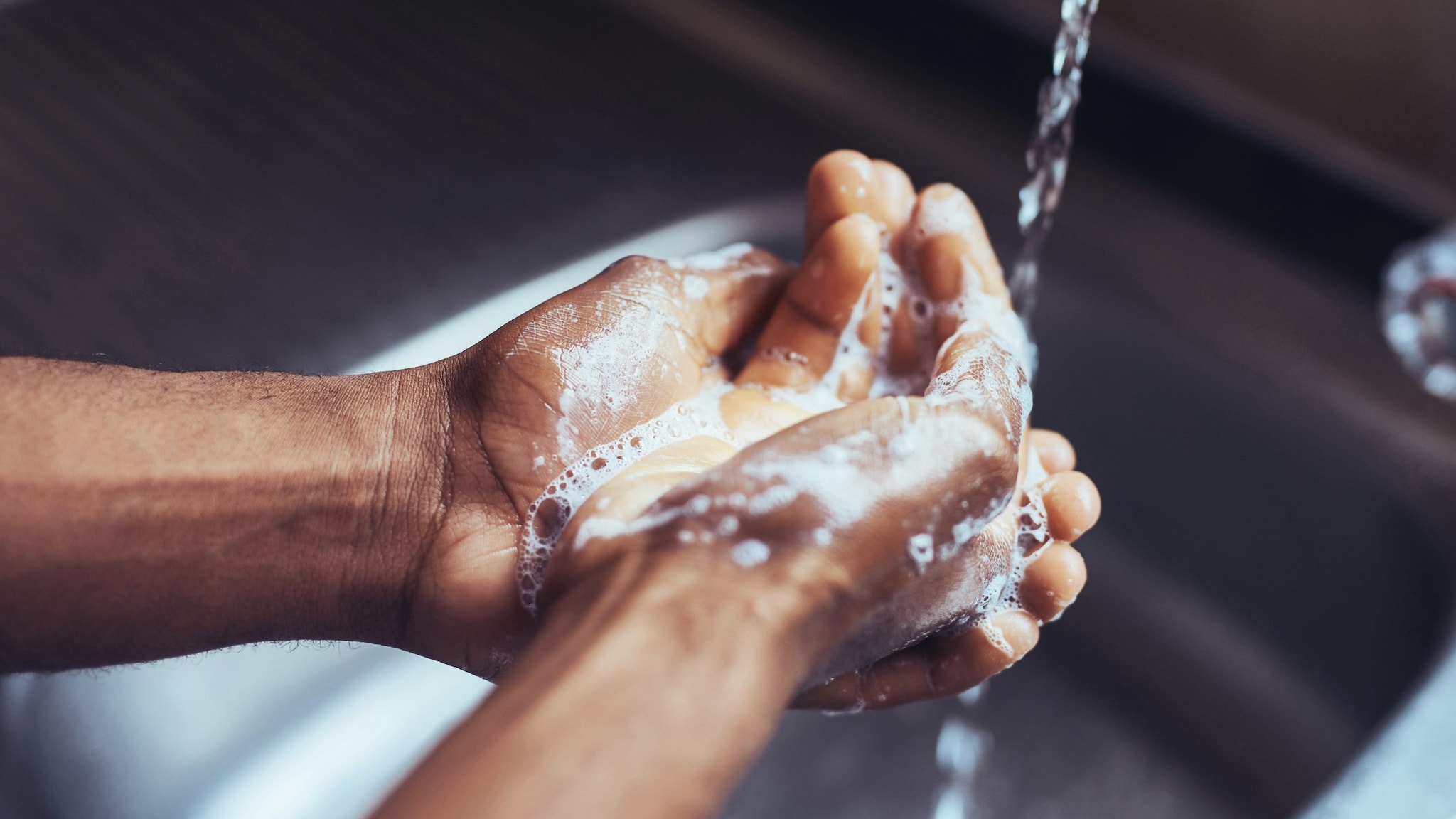 Closeup of soapy hands under water streaming from a faucet.