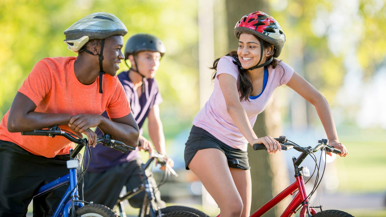 A group of teens riding their bikes in the park with helmets on.