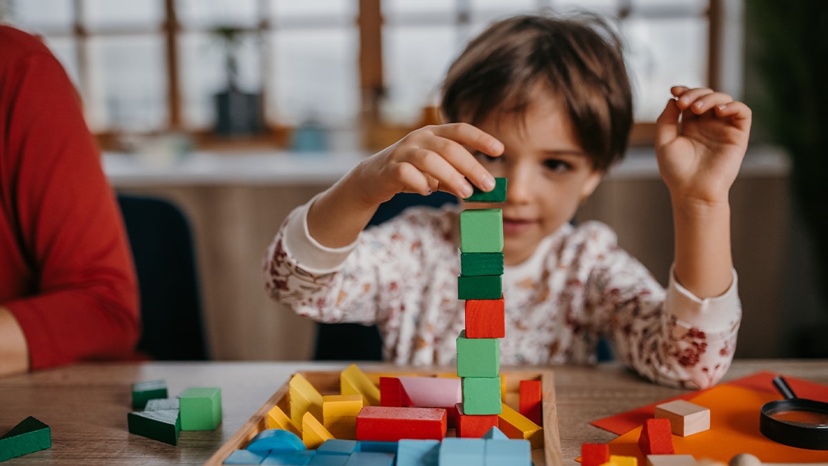 Niño jugando con bloques apilándolos uno sobre el otro.