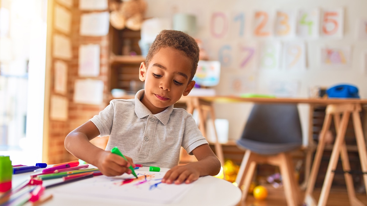 Niño escribiendo y coloreando en un salón de clases.