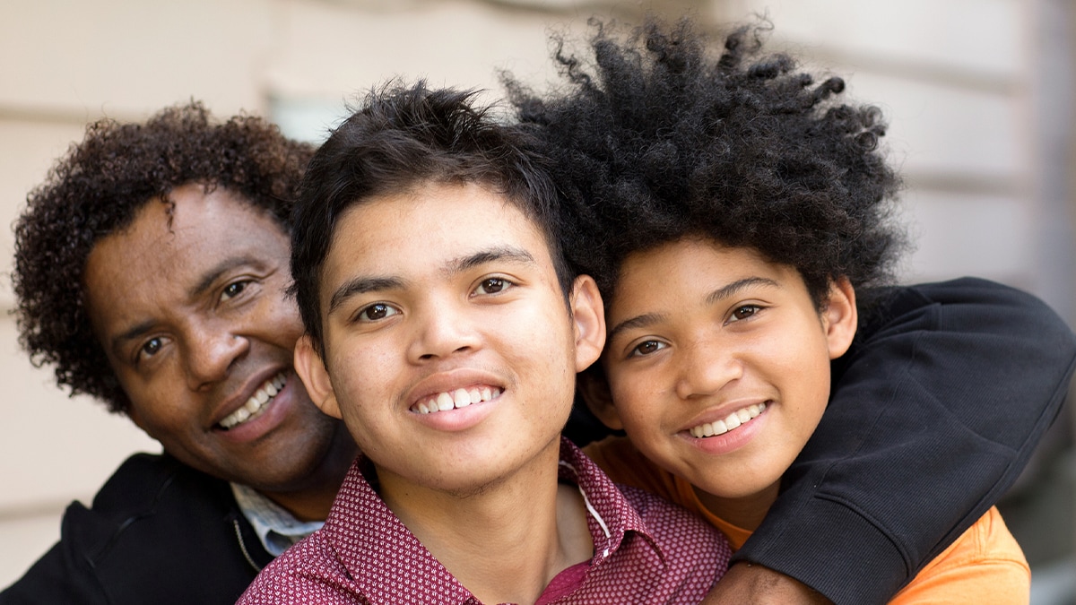 Father hugging his two sons while smiling together at camera