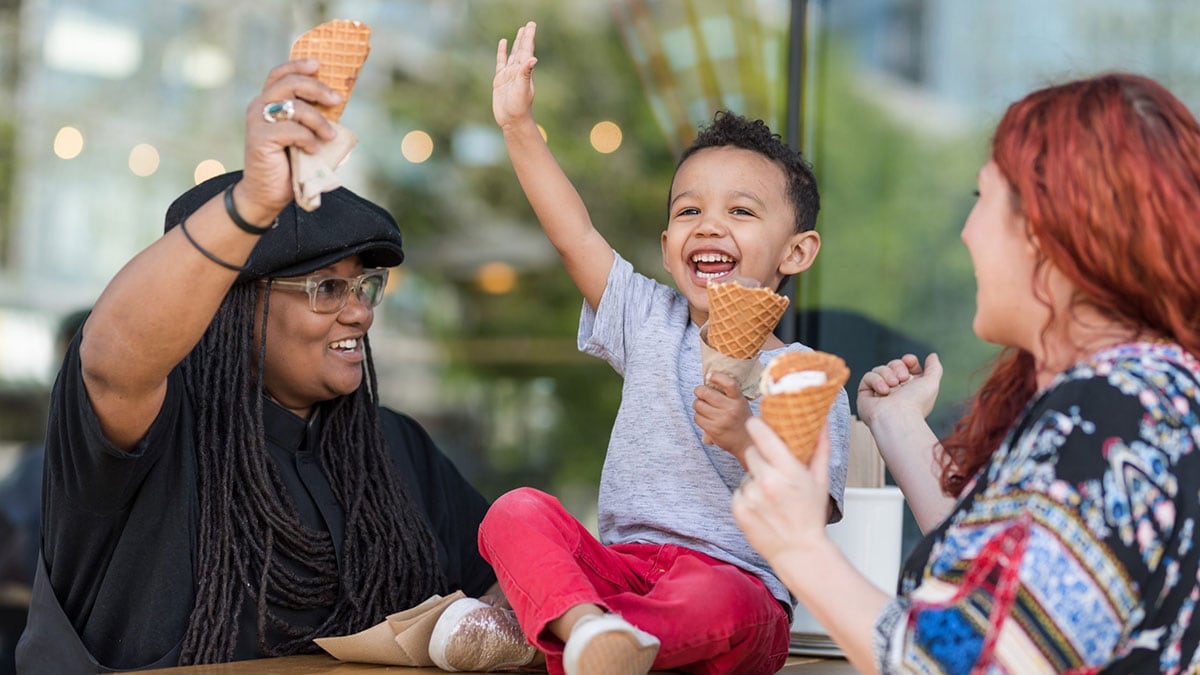 Niño pequeño comiendo helado felizmente con sus dos madres.