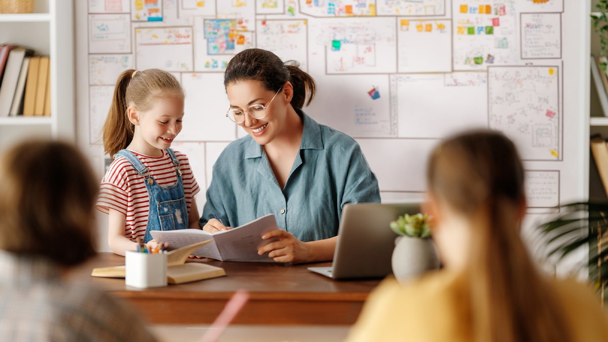 teacher at school with student looking at book