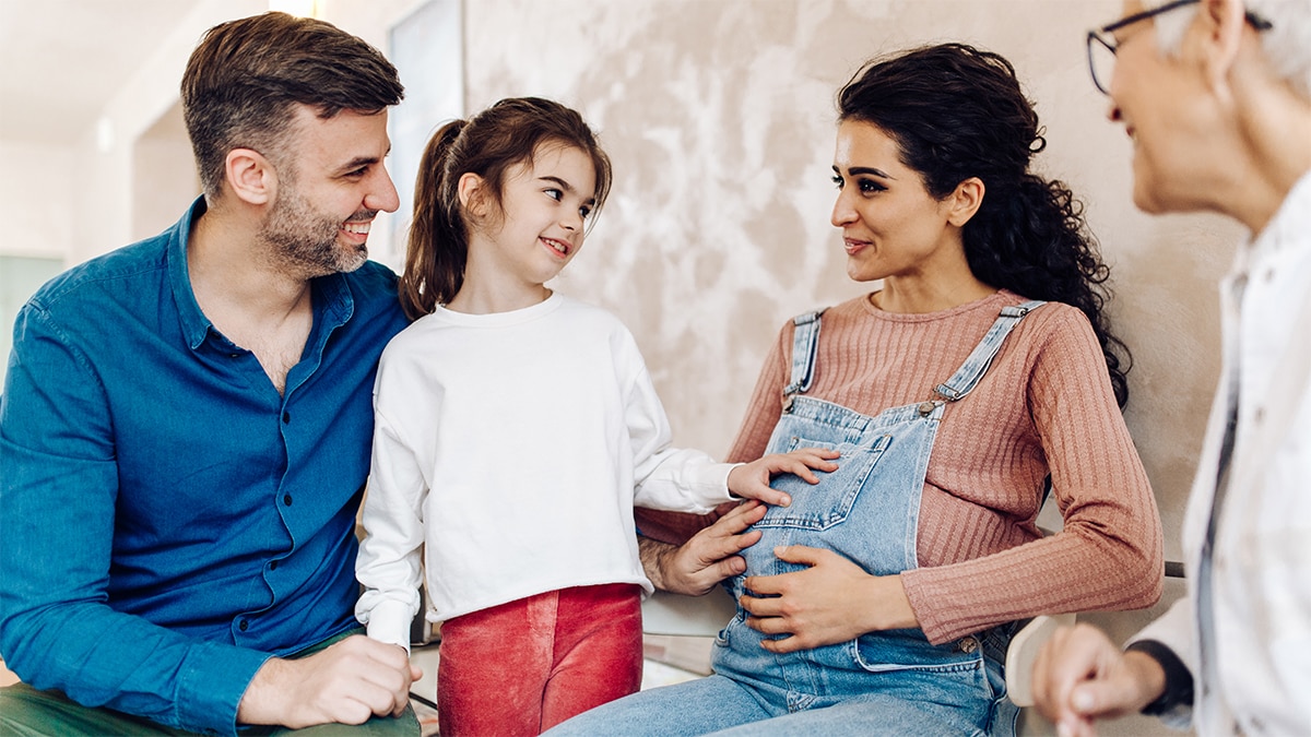 Multigenerational family smiling at each other, with the pregnant mom in the center.