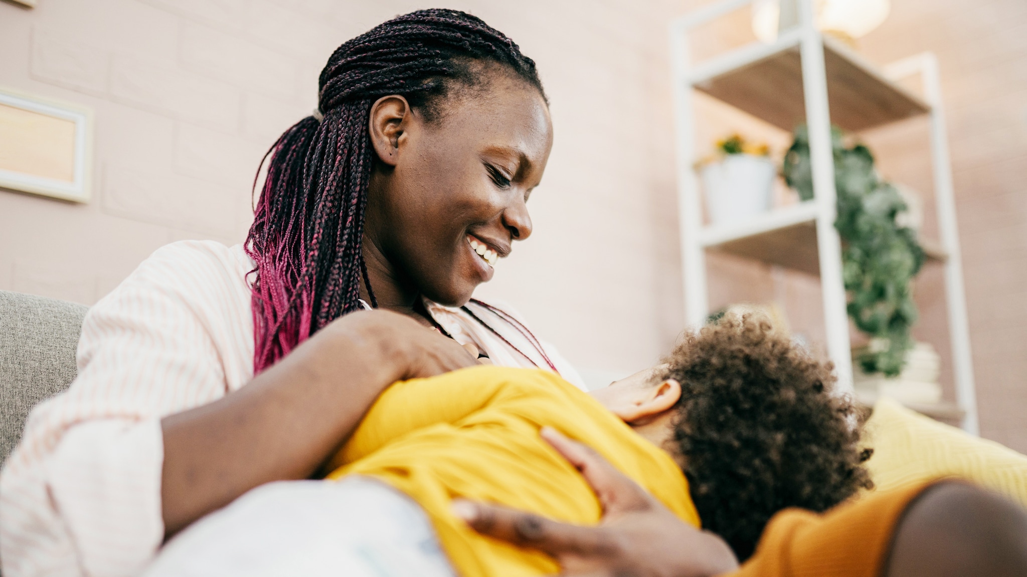 A mom smiles at her young child whom she cradles as the child breastfeeds.