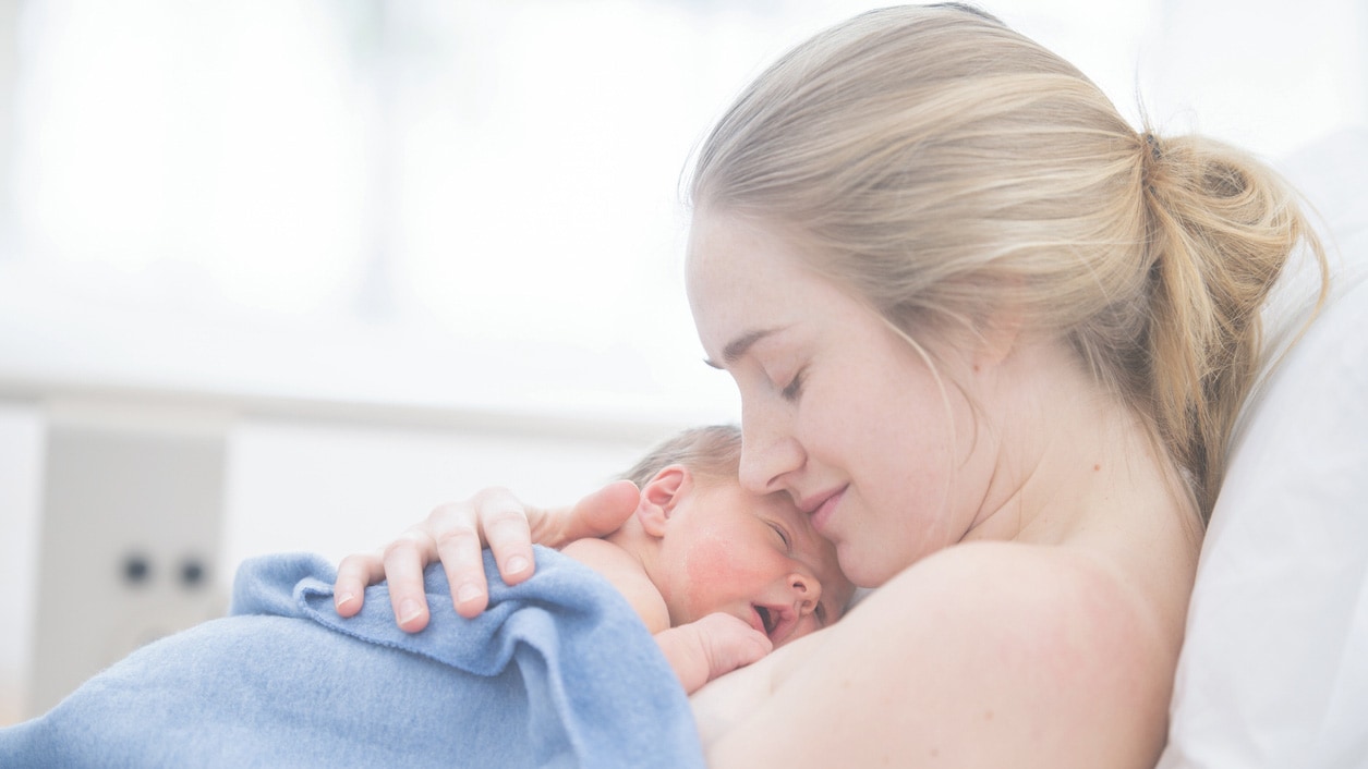 A mother is cradling her newborn baby. They are indoors in a hospital room.