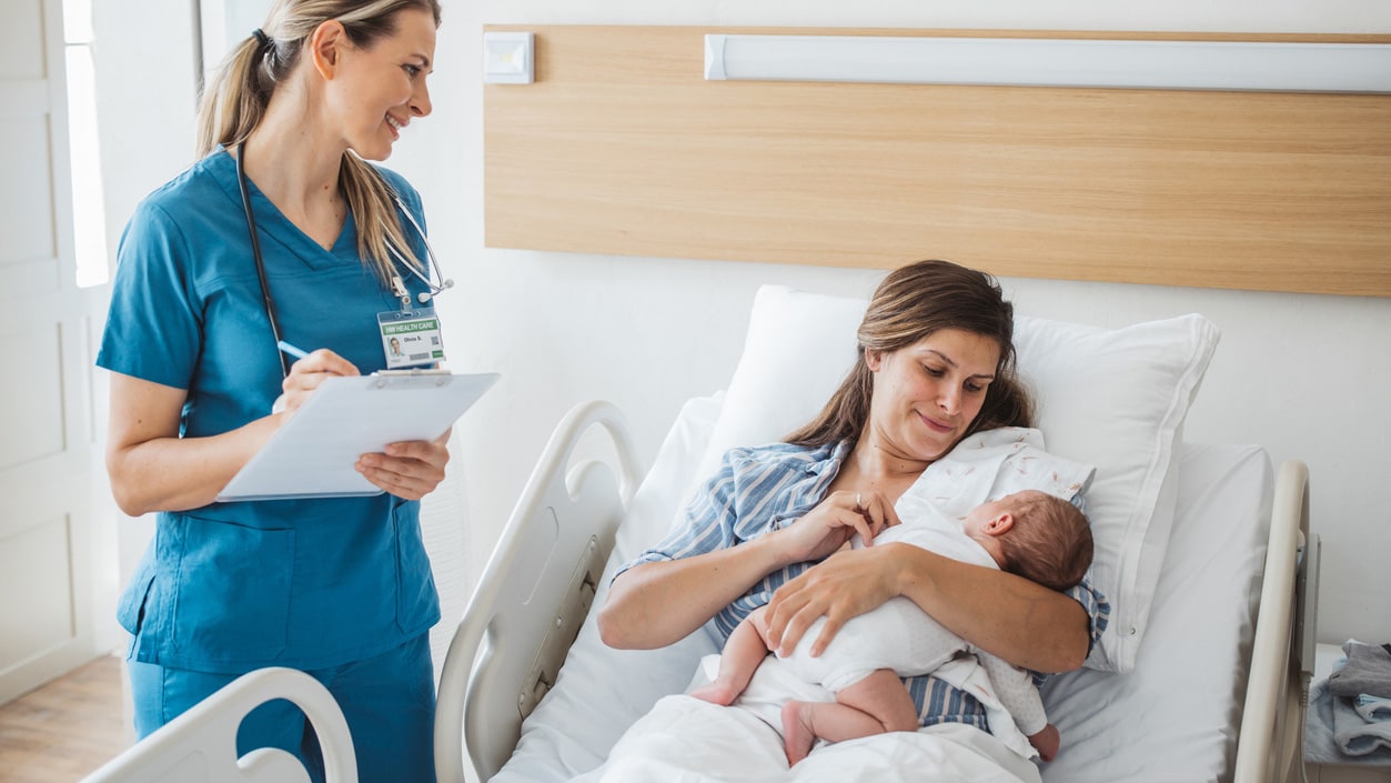 A nurse takes personal data from a mother and talks to her while she holds her newborn baby.