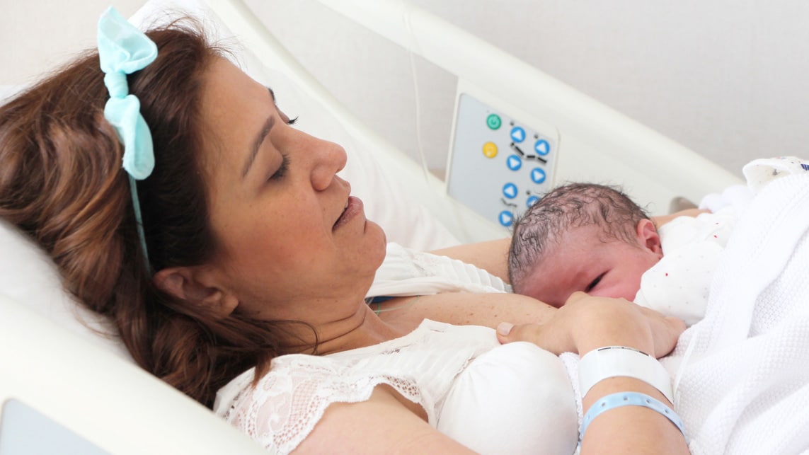 A mother nursing her newborn in hospital bed.