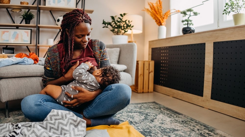 Mother sitting on the floor in a living room to breastfeed her child.