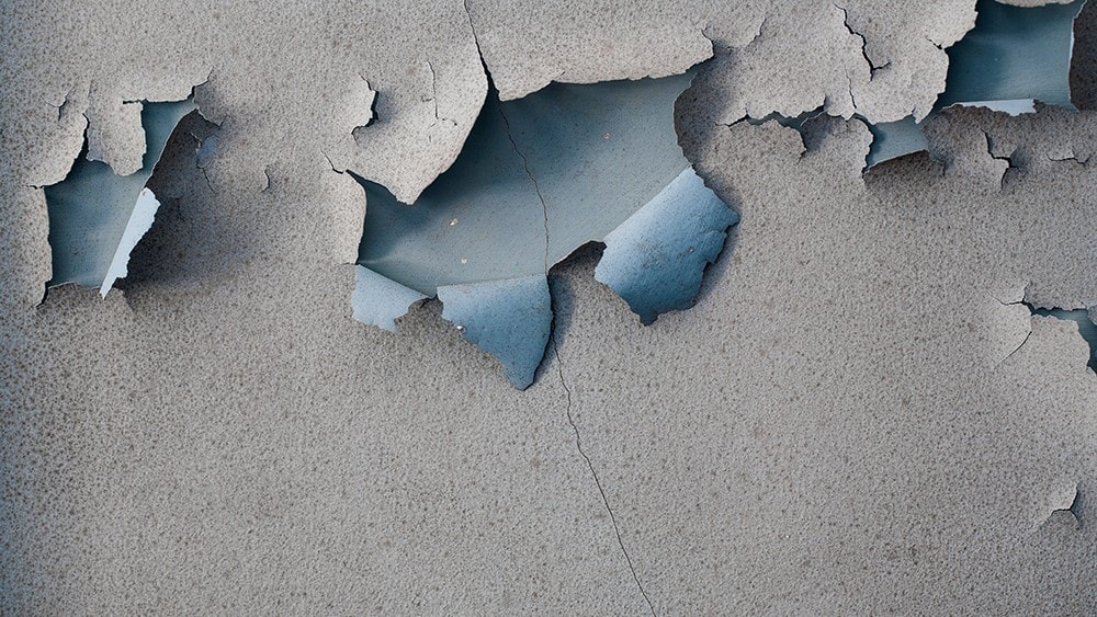 Grey paint paint peeling off a blue wall.