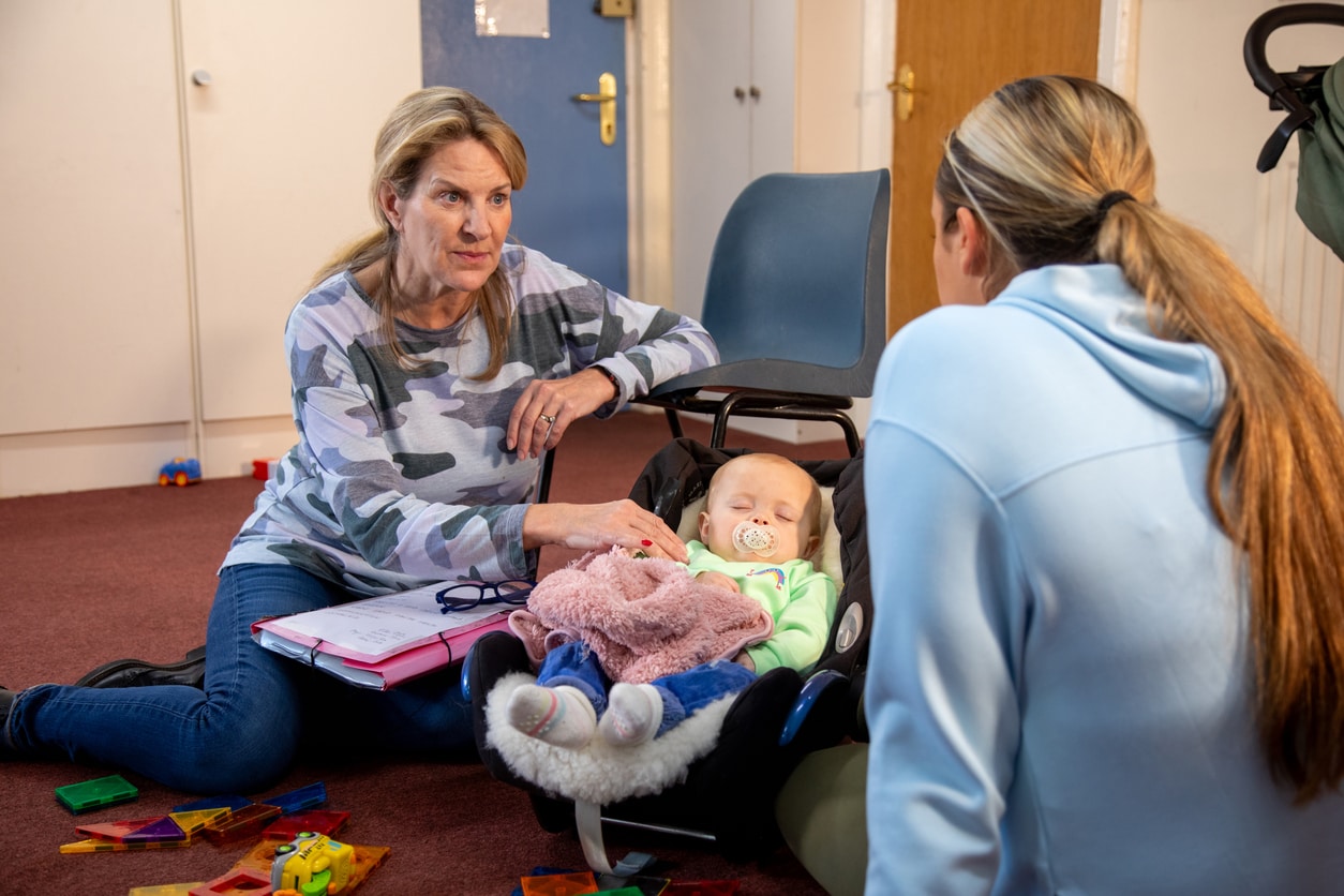 A mother and baby child having a meeting with a childcare worker.