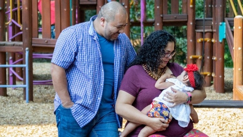 Man and woman at a park while woman breastfeeds a baby.