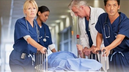 Group of healthcare providers pushing a patient on a stretcher through a hospital hallway.