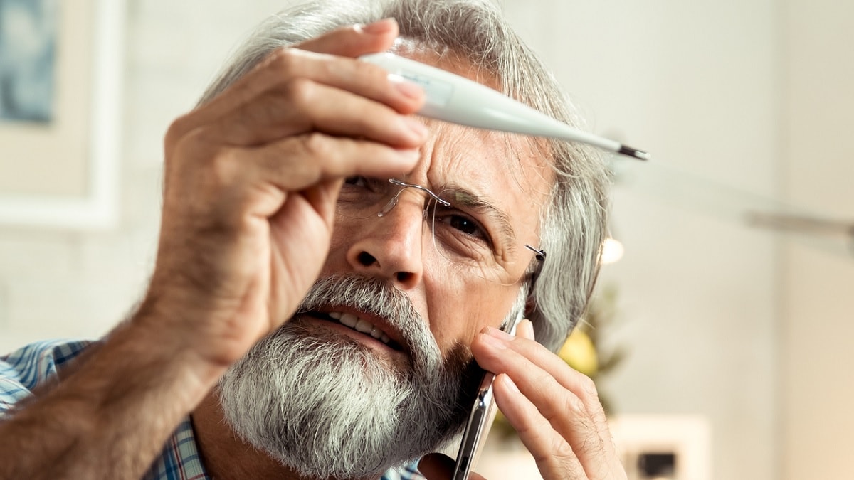 Photo of a man looking at a thermometer and calling his doctor