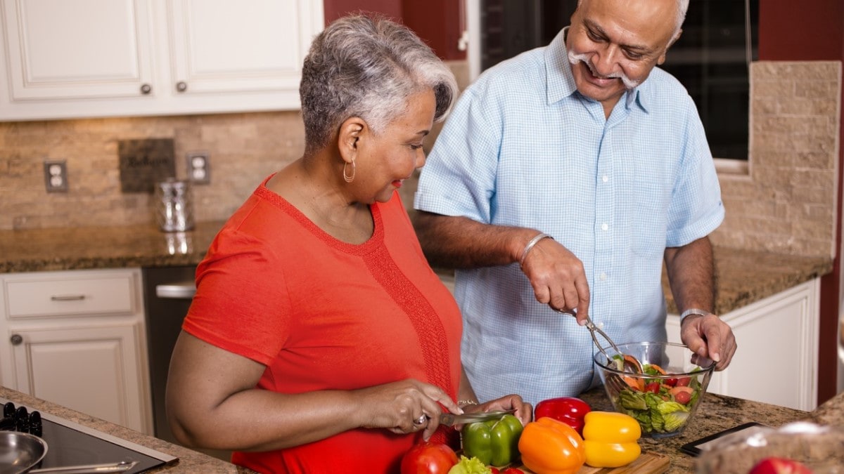 a couple in a kitchen making a salad