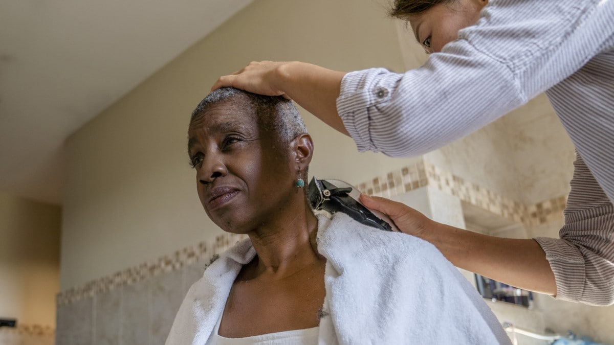 una mujer afeitando el cabello de una sobreviviente que enfrenta pérdida de cabello