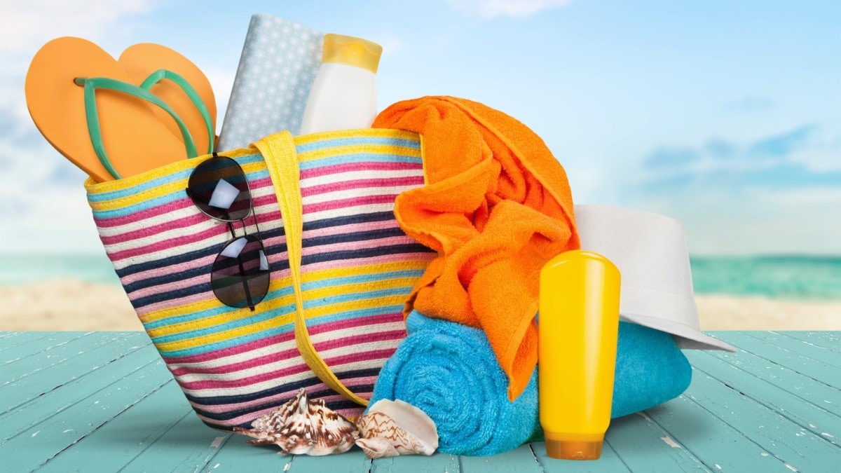 Foto de una bolsa de asas colorida que contiene protector solar, lentes oscuros, un sombrero, toallas y zapatos