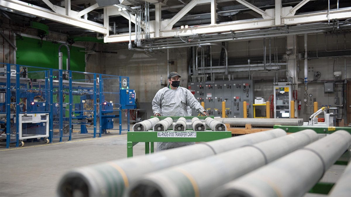 An image of a worker in personal protective equipment loading chemical munitions onto a conveyor.