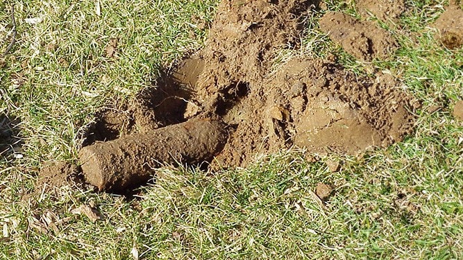 A chemical agent mortar lying in a shallow hole recently excavated.