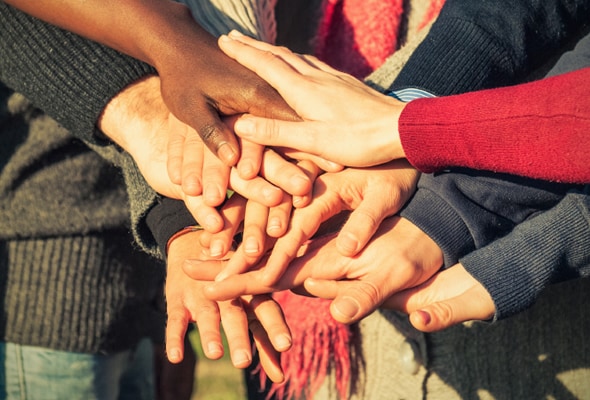 Photo of many people with their hands in the middle of a circle together.