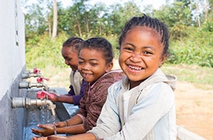 Three smiling children washing their hands