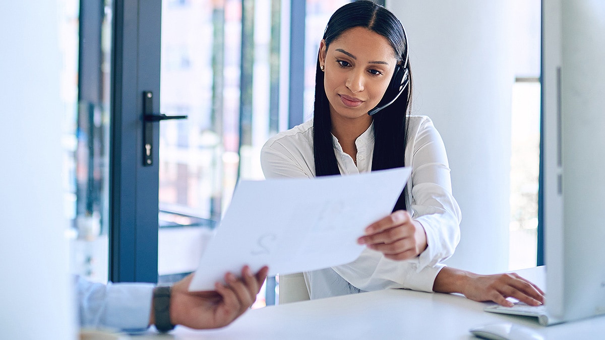 Woman wearing call headset being handed a document.