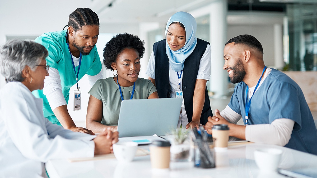 Diverse group of medical professionals all looking at a laptop in a meeting.