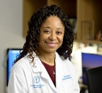 Esther Babady behind a desk, smiling, and wearing a white lab coat