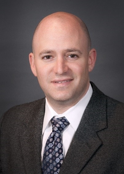 Studio headshot of Jordan Laser in a suit and tie.