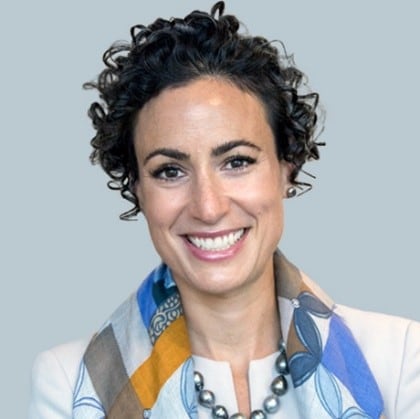 Dr. Heher's headshot. She has short, dark, curly hair wearing a multicolored scare, white suit jacket, and necklace.