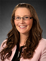 Collette Fitzgerald Leaumont's headshot. She has long brown hair, glasses, pink suit jacket, and a black shirt.