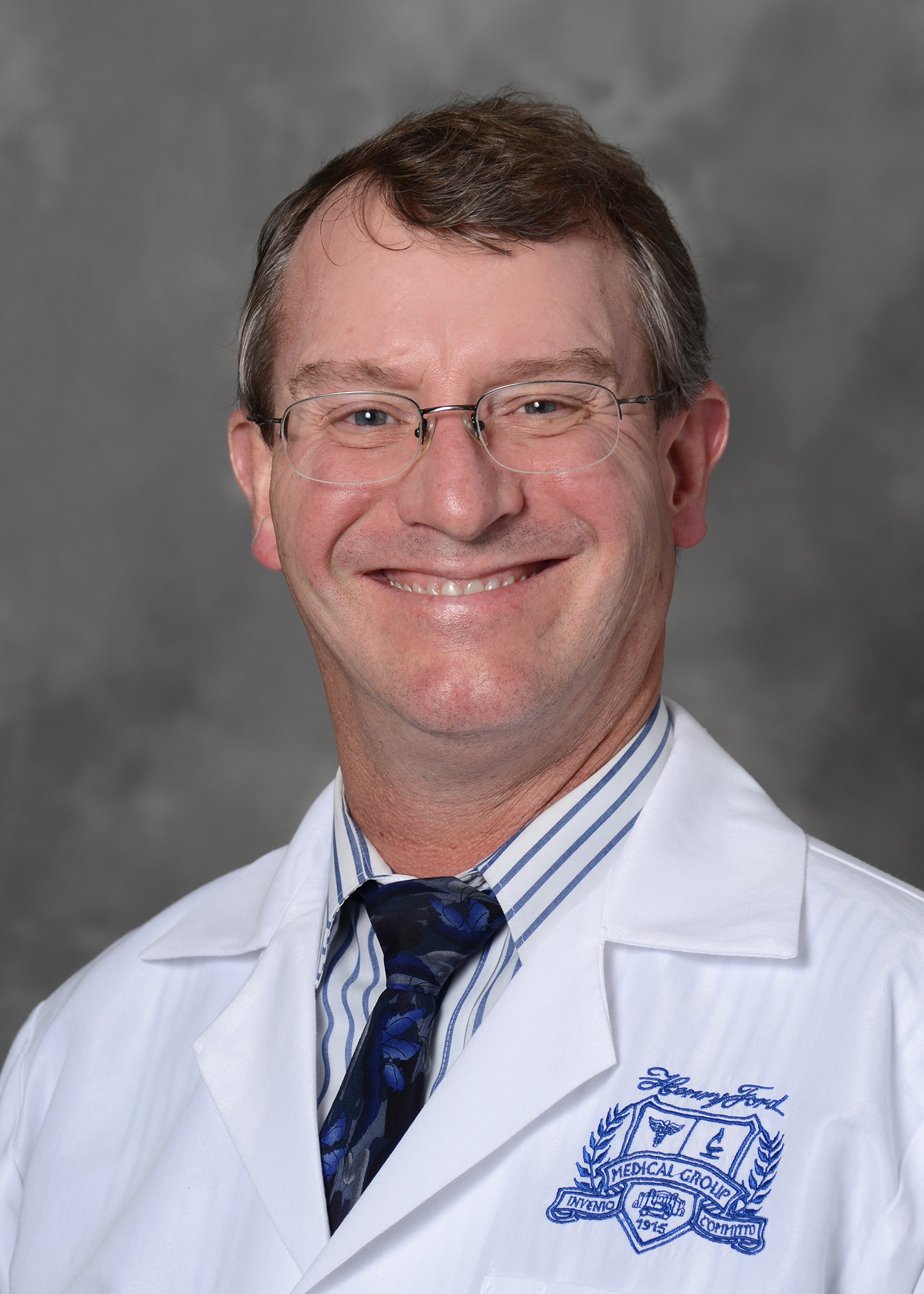 Dr. Tuthill's headshot. He is wearing a white lab coat, striped button up dress shirt, and blue tie.