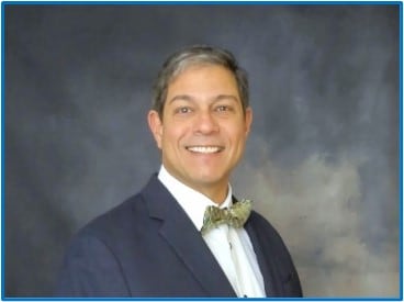 Profile picture of Víctor R. De Jesús, PhD. Brown and gray hair wearing a navy blazer and green bowtie.