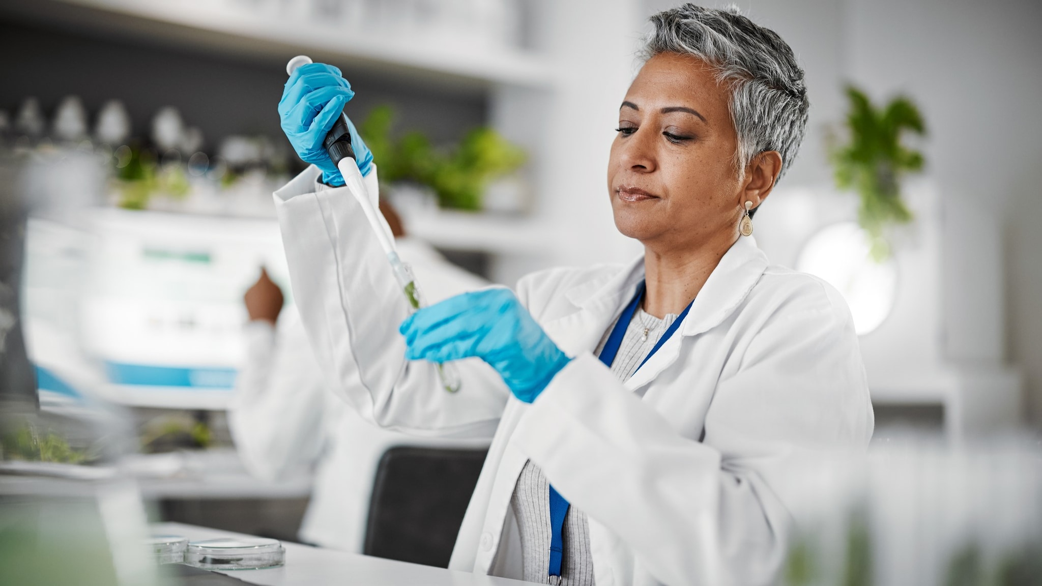 A laboratorian working in a laboratory. They are using a pipette and test tube, transferring liquid from one to the other.