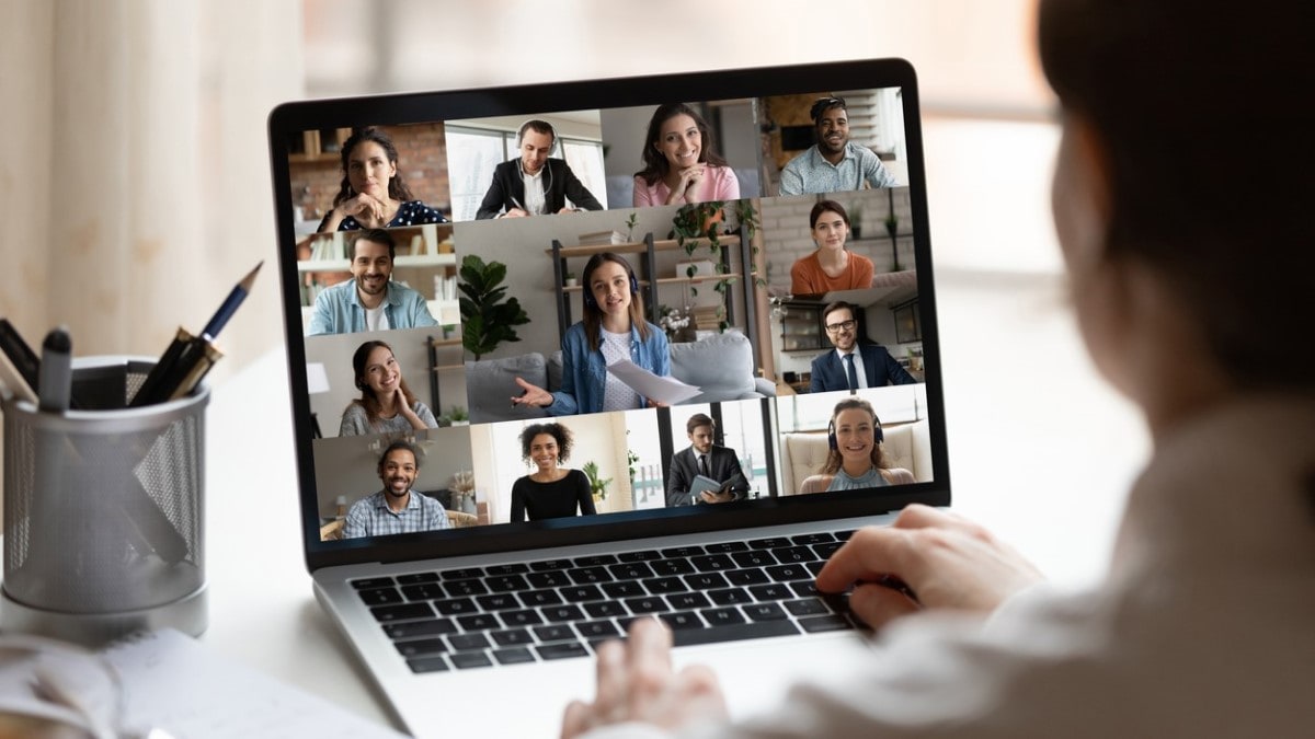 A person typing on a laptop while watching a virtual meeting