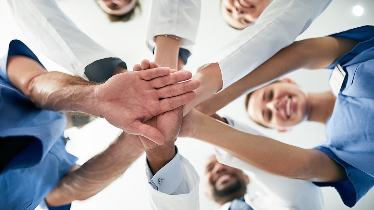 A group of medical professionals standing in a circle and joining their hands together in the middle