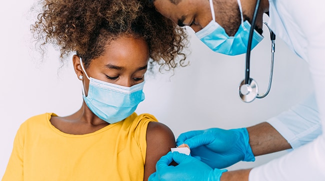 Proveedor de atención médica aplicando una curita al brazo de una niña.