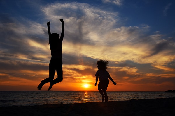 Los miembros de una familia joven y feliz se divierten en la playa y saltan al atardecer.