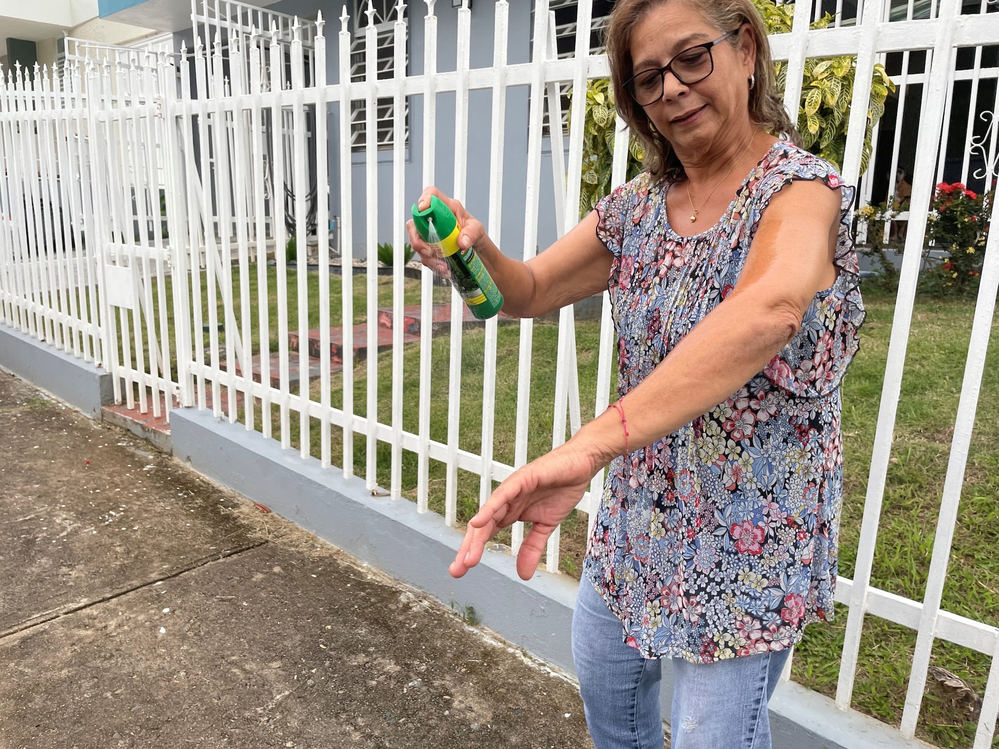 Una mujer mayor rociándose repelente de insectos en el brazo.