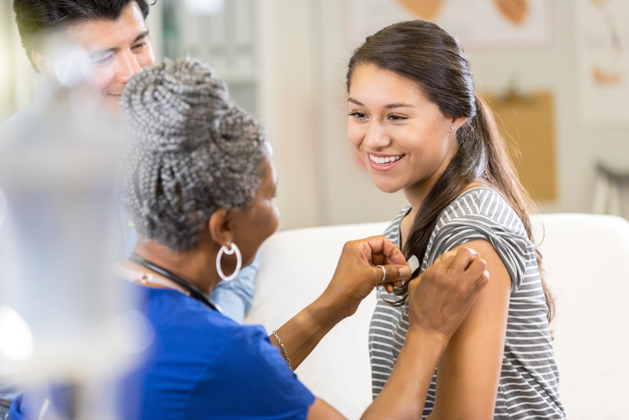 Healthcare provider applying a bandage to a pediatric patient's arm as a parent looks on.