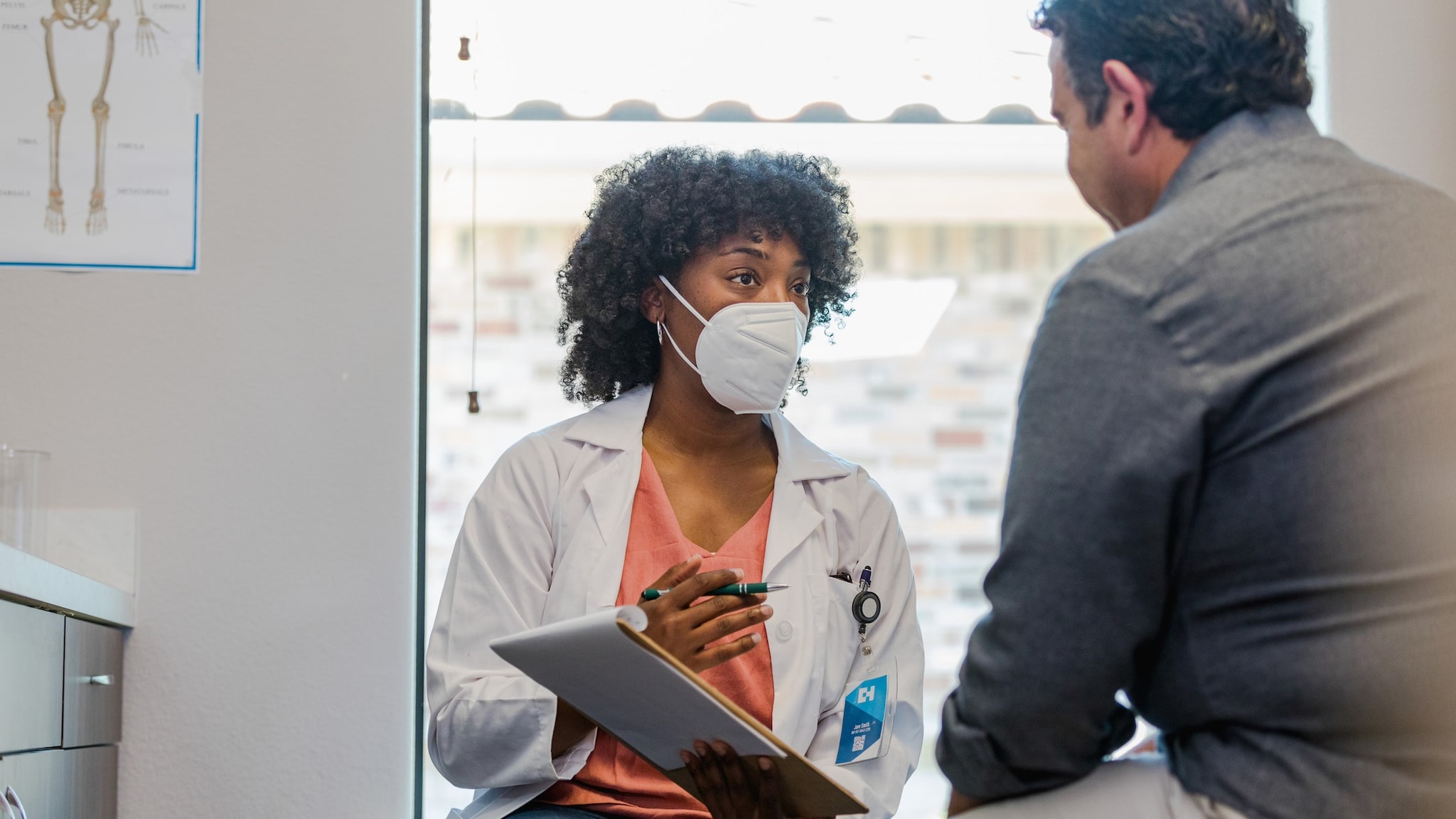 A doctor wearing a mask talking to a patient