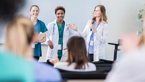 Women in white coats speaking to an audience